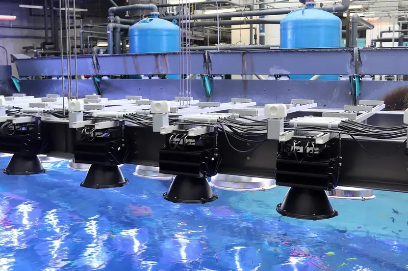 Rows of light fixtures mounted above a large aquarium tank, with pipework behind